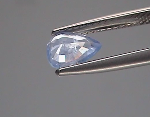 Faceted gemstone held by tweezers against a gray background