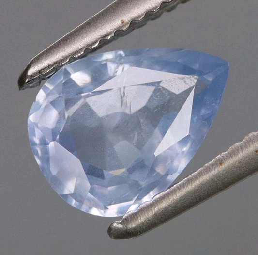 Trillion-cut blue gemstone held by tweezers against a gray background