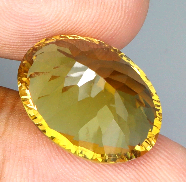 Faceted yellow gemstone held between fingers against a neutral background
