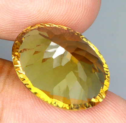 Faceted yellow gemstone held between fingers against a neutral background
