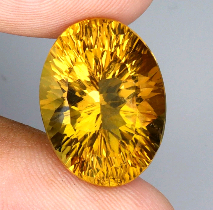 Yellow gemstone held between fingers against a neutral background