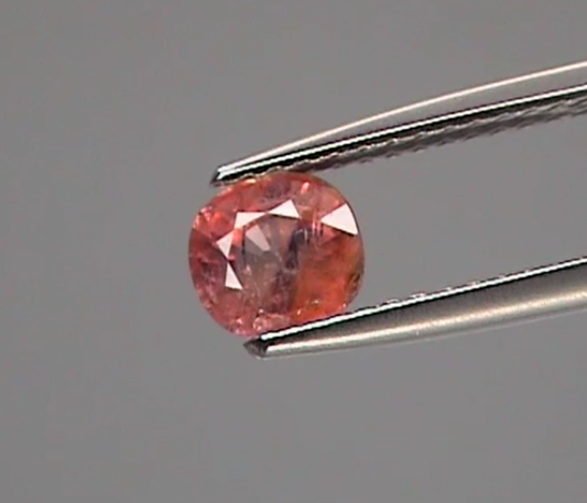 Pink gemstone held by tweezers against a gray background