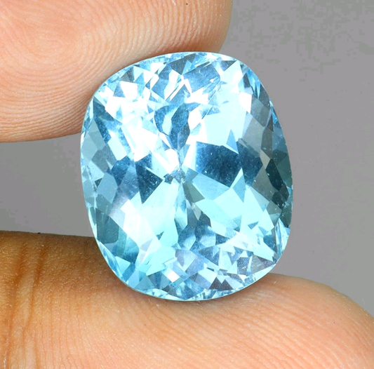 Blue gemstone held between fingers against a neutral background