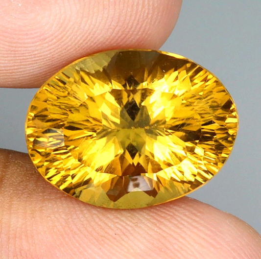 Large yellow gemstone held between fingers against a neutral background