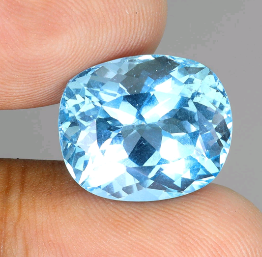 Blue gemstone held between fingers against a neutral background