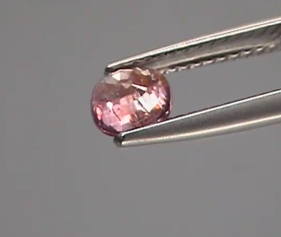 Pink gemstone held by tweezers against a gray background