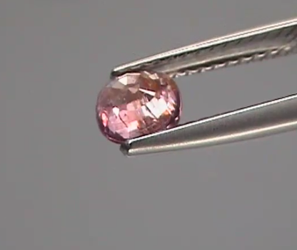 Pink gemstone held by tweezers against a gray background