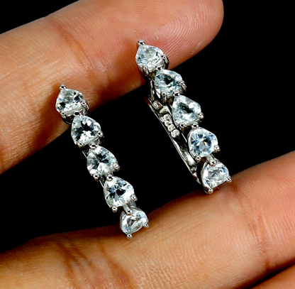 Pair of silver earrings with clear gemstones held between fingers against a dark background
