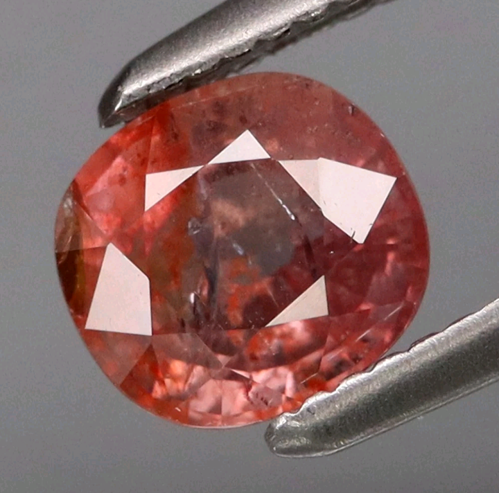 Red gemstone held between tweezers against a gray background