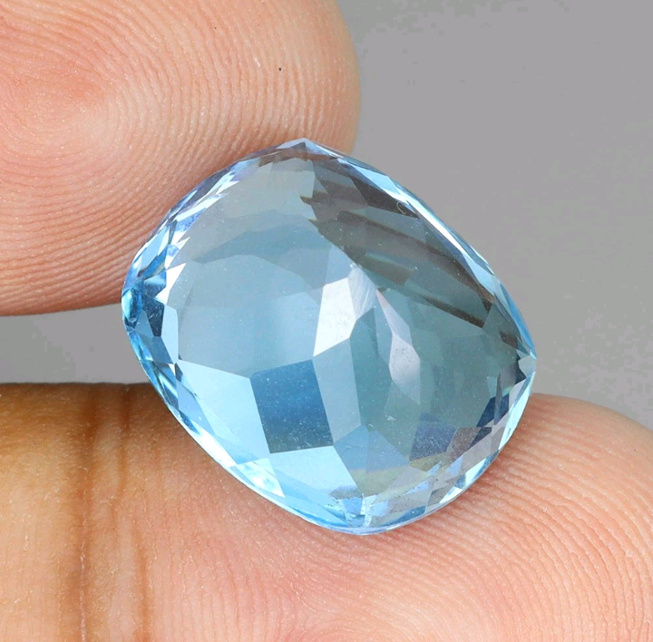 Faceted blue gemstone held between fingers against a neutral background