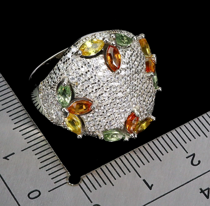 Silver ring with colorful gemstones on a black background with a ruler for scale.